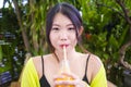 Young attractive and happy Asian Chinese girl having fun in garden outdoors drinking healthy orange juice with straw playful Royalty Free Stock Photo