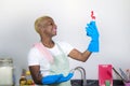 Young attractive and happy black afro american woman cleaning home kitchen holding detergent spray bottle wearing washing rubber Royalty Free Stock Photo
