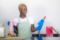 Young attractive and happy black afro american woman cleaning home kitchen holding detergent spray bottle wearing washing rubber Royalty Free Stock Photo