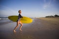 Young attractive and happy blonde surfer girl in beautiful beach carrying yellow surf board running out of the sea enjoying summer Royalty Free Stock Photo