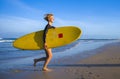 Young attractive and happy blonde surfer girl in beautiful beach carrying yellow surf board running out of the sea enjoying summer Royalty Free Stock Photo