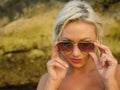 Young attractive happy and cheerful blond girl in bikini smiling playful holding sunglasses posing carefree at beautiful beach