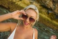 Young attractive happy and cheerful blond girl in bikini smiling playful holding sunglasses posing carefree at beautiful beach