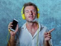 Young attractive and happy cool man listening to music song with yellow headphones using internet mobile phone dancing in trance s Royalty Free Stock Photo