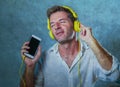 Young attractive and happy cool man listening to music song with yellow headphones using internet mobile phone dancing in trance s Royalty Free Stock Photo