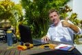 Young attractive and happy digital nomad man working outdoors from coffee shop with laptop computer giving thumb up relaxed and co Royalty Free Stock Photo