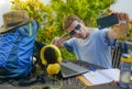 Young attractive and happy digital nomad man working outdoors with laptop computer cheerful taking selfie pic with mobile phone