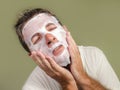 Young attractive and happy gay man in bathroom using beauty paper facial mask touching his face looking to the mirror smiling in Royalty Free Stock Photo