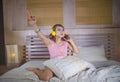 Young attractive and happy girl in bed with yellow headphones listening to music on internet with mobile phone dancing and singing Royalty Free Stock Photo