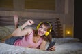 Young attractive and happy girl in bed with yellow headphones listening to music on internet with mobile phone dancing and singing Royalty Free Stock Photo