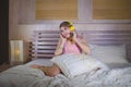 Young attractive and happy girl in bed with yellow headphones listening to music on internet with mobile phone dancing and singing Royalty Free Stock Photo