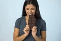 Young attractive and happy hispanic woman in blue top smiling excited eating chocolate bar background Royalty Free Stock Photo