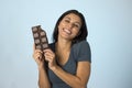 Young attractive and happy hispanic woman in blue top smiling excited eating chocolate bar background