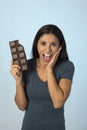 Young attractive and happy hispanic woman in blue top smiling excited eating chocolate bar background