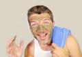 Young attractive and happy man with bathroom towel laughing of himself in the mirror with green cream on his face applying facial Royalty Free Stock Photo