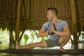 Young attractive and happy man doing yoga drill and stretching exercise smiling relaxed in harmony at beautiful Asian bamboo hut Royalty Free Stock Photo