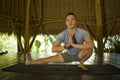 Young attractive and happy man doing yoga drill and stretching exercise smiling relaxed in harmony at beautiful Asian bamboo hut Royalty Free Stock Photo