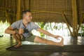 Young attractive and happy man doing yoga drill and stretching exercise smiling relaxed in harmony at beautiful Asian bamboo hut Royalty Free Stock Photo