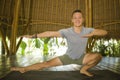 Young attractive and happy man doing yoga drill and stretching exercise smiling relaxed in harmony at beautiful Asian bamboo hut Royalty Free Stock Photo