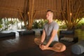 Young attractive and happy man doing yoga sitting in lotus position meditating relaxed in harmony at beautiful Asian bamboo hut Royalty Free Stock Photo