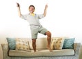 Young attractive and happy man with headphones and mobile phone listening to music jumped on sofa couch dancing and singing crazy Royalty Free Stock Photo