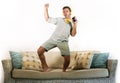 Young attractive and happy man with headphones and mobile phone listening to music jumped on sofa couch dancing and singing crazy Royalty Free Stock Photo