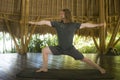 Young attractive and happy man in hipster yogi style doing yoga drill on mat at beautiful Asian bamboo hut stretching body Royalty Free Stock Photo