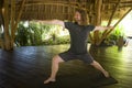 Young attractive and happy man in hipster yogi style doing yoga drill on mat at beautiful Asian bamboo hut stretching body Royalty Free Stock Photo