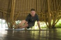 Young attractive and happy man in hipster yogi style doing yoga drill on mat at beautiful Asian bamboo hut stretching body Royalty Free Stock Photo