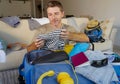Young attractive and happy man at home couch preparing travel back and packing suitcase folding clothes and organizing passport an Royalty Free Stock Photo