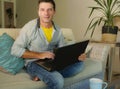 Young attractive and happy man at home relaxed working on laptop computer sitting at living room sofa couch smiling cheerful as in Royalty Free Stock Photo