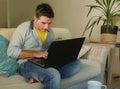 Young attractive and happy man at home relaxed working on laptop computer sitting at living room sofa couch smiling cheerful as in Royalty Free Stock Photo