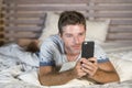 Young attractive and happy man lying on bed using internet mobile phone smiling sending text in social media and cellular communic Royalty Free Stock Photo