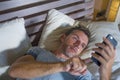 Young attractive and happy man lying on bed using internet mobile phone smiling sending text in social media and cellular communic Royalty Free Stock Photo