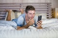 Young attractive and happy man lying on bed using internet mobile phone smiling sending text in social media and cellular communic Royalty Free Stock Photo