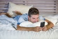 Young attractive and happy man lying on bed using internet mobile phone smiling sending text in social media and cellular communic Royalty Free Stock Photo