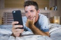 Young attractive and happy man lying on bed using internet mobile phone smiling sending text in social media and cellular communic