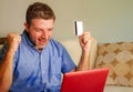 Young attractive and happy man relaxed at home sofa couch using credit card and laptop computer for internet shopping and banking Royalty Free Stock Photo