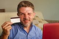 Young attractive and happy man relaxed at home sofa couch using credit card and laptop computer for internet shopping and banking Royalty Free Stock Photo