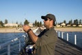 Young attractive and happy man in shirt and hat fishing at beach sea dock using fish road enjoying weekend hobby in holidays Royalty Free Stock Photo