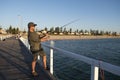 Young attractive and happy man in shirt and hat fishing at beach sea dock using fish road enjoying weekend hobby in holidays Royalty Free Stock Photo