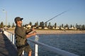 Young attractive and happy man in shirt and hat fishing at beach sea dock using fish road enjoying weekend hobby in holidays Royalty Free Stock Photo