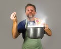 Young attractive happy and proud home cook man cooking soup holding kitchen pot smelling the meal aroma gesturing delighted and sa Royalty Free Stock Photo