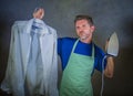 Young attractive happy and proud house husband or single man holding iron showing shirt after ironing on studio backgroun