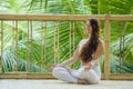 Young attractive and happy relaxed woman doing yoga and meditation exercise sitting in lotus position outdoors at wooden hut