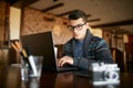 Young Attractive Hipster Man In Glasses And Winter Sweater Working On Laptop In Cafe. Freelancer Businessman Browsing