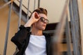 Young attractive hipster man straightens trendy black sunglasses. Portrait of a stylish handsome guy in a black vintage shirt Royalty Free Stock Photo