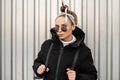 Young attractive hipster woman with stylish hairstyle with a bandana in black glasses in a long black coat with a backpack Royalty Free Stock Photo