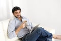 Young attractive Hispanic man at home on white couch using digital tablet or pad Royalty Free Stock Photo