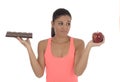 Young attractive hispanic woman in fitness top holding apple fruit and chocolate bar in her hands Royalty Free Stock Photo